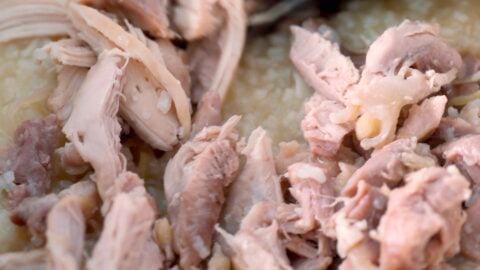 Stirring shredded chicken into Arroz Caldo.