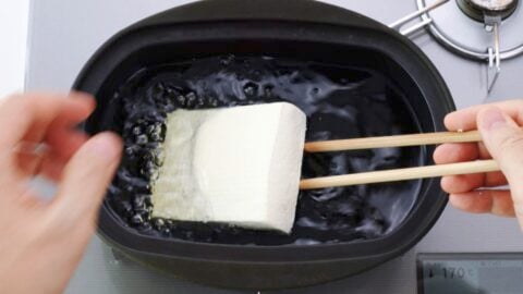 Lowering tofu into frying oil to make atsuage.