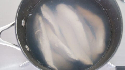 Chicken tenders poaching in a pot of hot water.