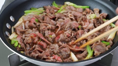 Thinly sliced beef for niku udon cooking in broth.