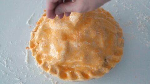 Sprinkling raw sugar onto the top crust of an egg washed apple pie.