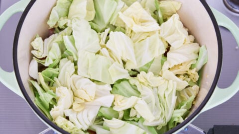 Pieces of cabbage in a green dutch oven.