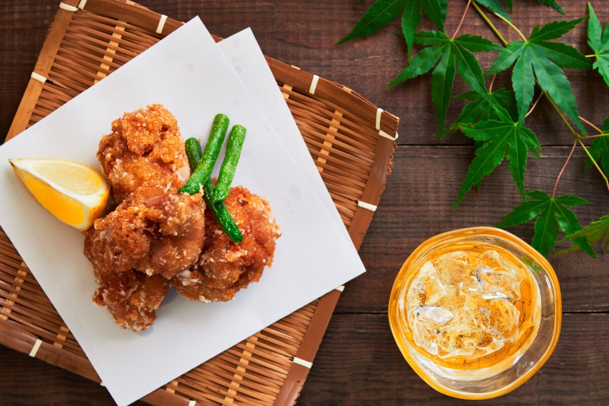 Crispy Chicken Karaage (Japanese Fried Chicken) presented in a basket with Japanese maple leaves and a glass of shochu.