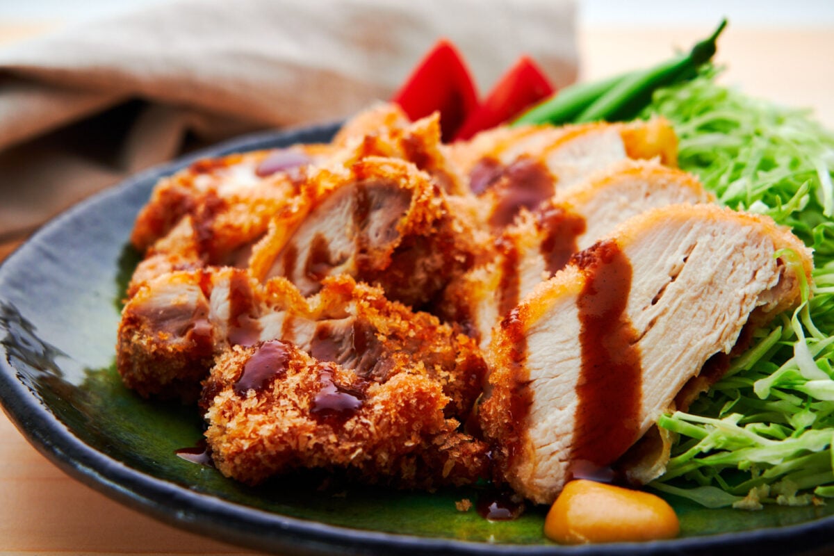 Japanese chicken katsu on a green plate with shredded cabbage and tomatoes.