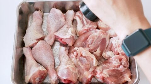 Chicken drumsticks and thighs being seasoned with black pepper.