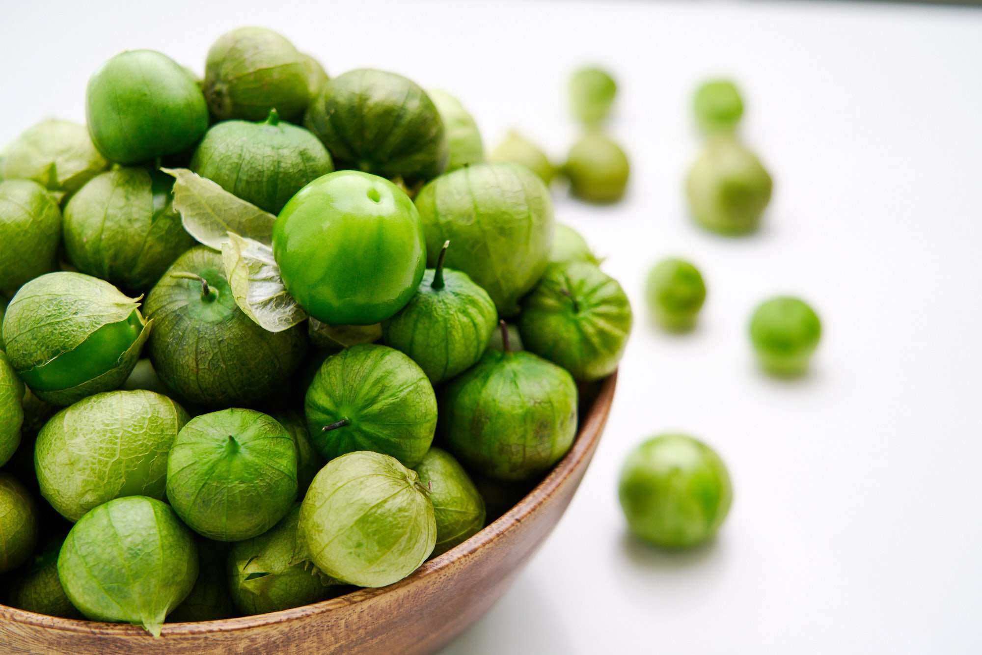 A wooden bowl overflowing with fresh tomatillos.