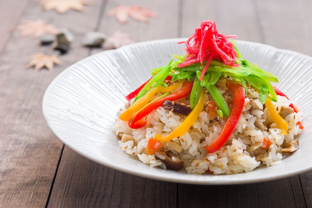 A bowl of fragrant sushi rice, cooked with shiitake mushrooms, and topped with colorful vegetables. 