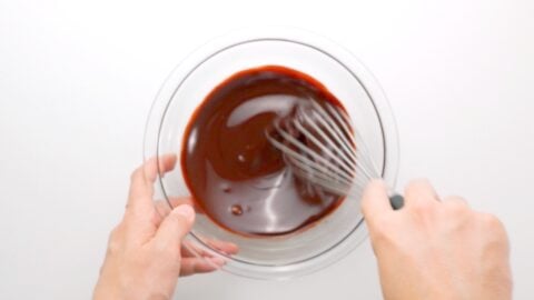 Whisking melted butter and chocolate together in a glass bowl.