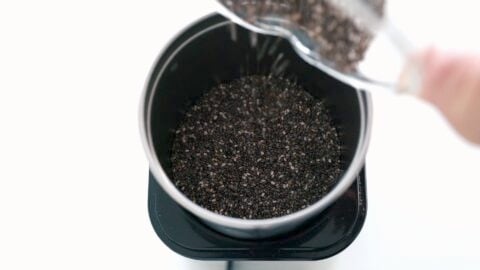 Adding chia seeds into a coffee grinder to make vegan chocolate pudding.