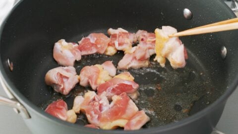 Browning chicken thighs in a frying pan for curry udon.