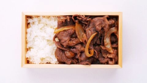 Packing Gyunabe on rice in a wooden bento box.