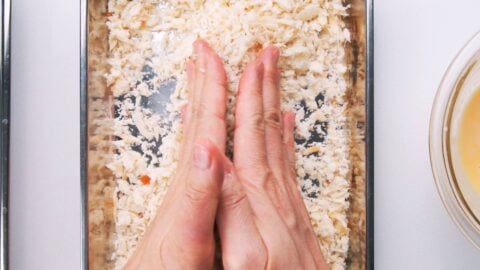 Pressing panko onto shrimp with hands.