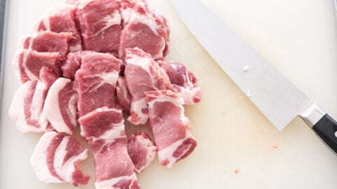 Pork shoulder sliced for making tocino with a knife on a cutting board.