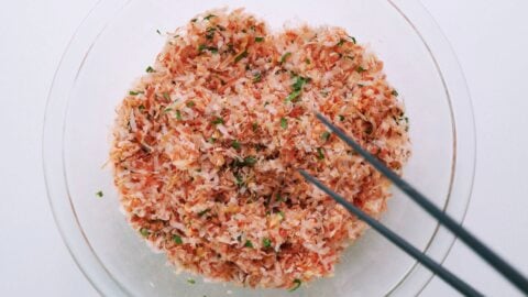 Mixing katsuobushi, sesame seeds and spinach in a glass bowl with chopsticks.