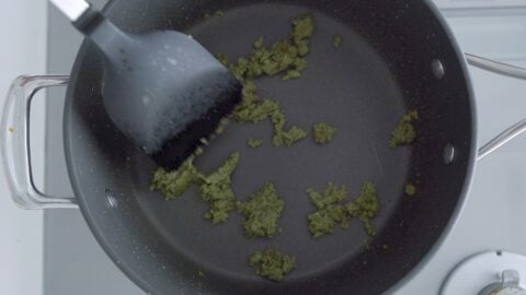 Frying green curry paste in a pot with a black spatula.