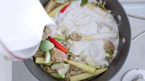 Adding baby corn, eggplant, chilies, bamboo, and coconut milk to green curry.