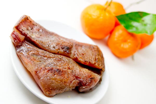 A piece of guanciale on a plate with mandarin oranges behind