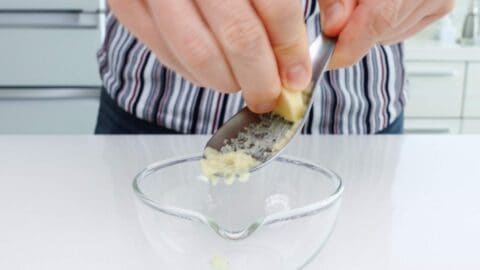 Grating ginger into a small glass bowl.