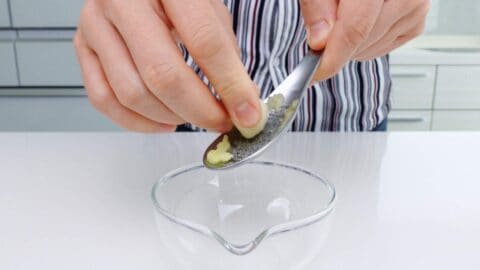 Grating garlic into a small glass bowl.