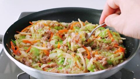 Tasting Japanese spring roll filling from a frying pan.