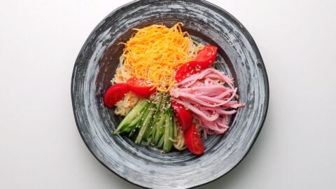 Plated Hiyashi Chuka with tomatoes, cucumbers, ham, Usuyaki Tamago, and chilled ramen noodles.