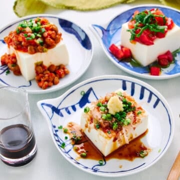 A wider shot of traditional Japanese Hiyayakko or cold tofu salad. In the background are two alternative versions - kimchi natto and Caprese Salad.