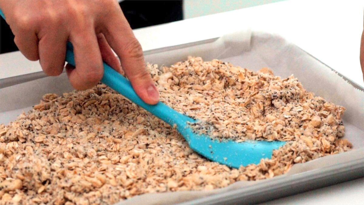 Compressing the granola using a spatula so that it forms clusters.