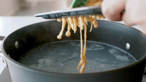 Forming Hungarian Nokedli into a boiling water using the back of a cheese grater.