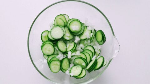 Cucumbers and onions salting in a glass bowl.