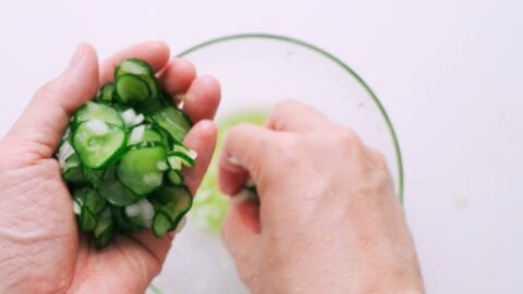 Hand squeezing salted cucumbers and onions.