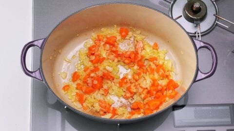 Onions and carrots browning in a dutch oven to make Japanese pumpkin soup.