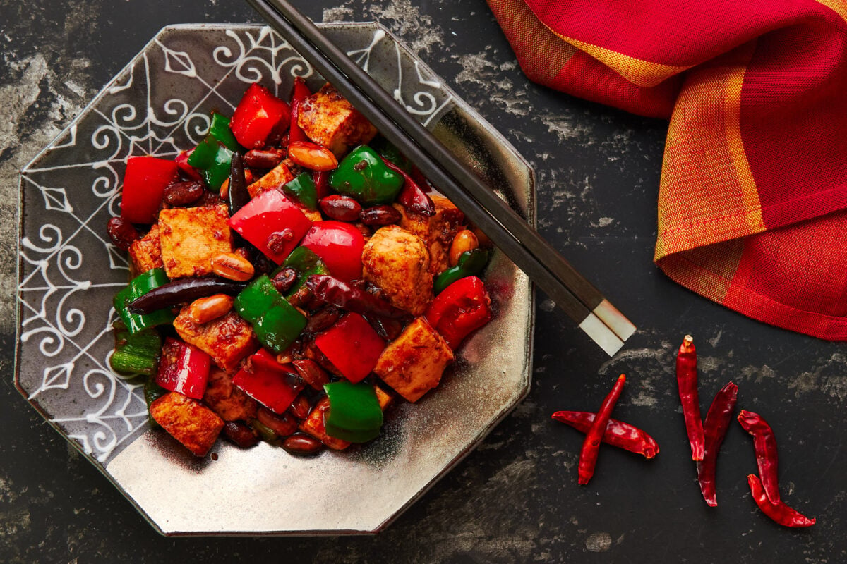 Vegan Kung Pao Tofu on a silver plate with chopsticks and a red and yellow napkin.