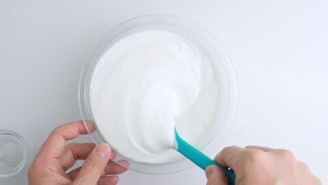 Mixing salt into yogurt with a blue spatula in a glass bowl.