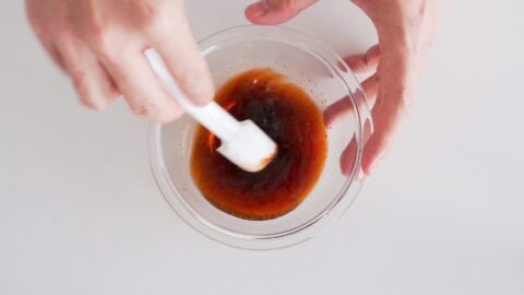 Mixing sauce for Lomo Saltado in a glass bowl with a white spatula