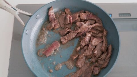 Stir-frying marinated beef in a frying pan.