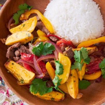 With tender beef marinated in soy sauce and pisco, Lomo Saltado is a delicious Peruvian-Chinese stir-fry that's loaded with potatoes, onions, tomatoes, and garlic.