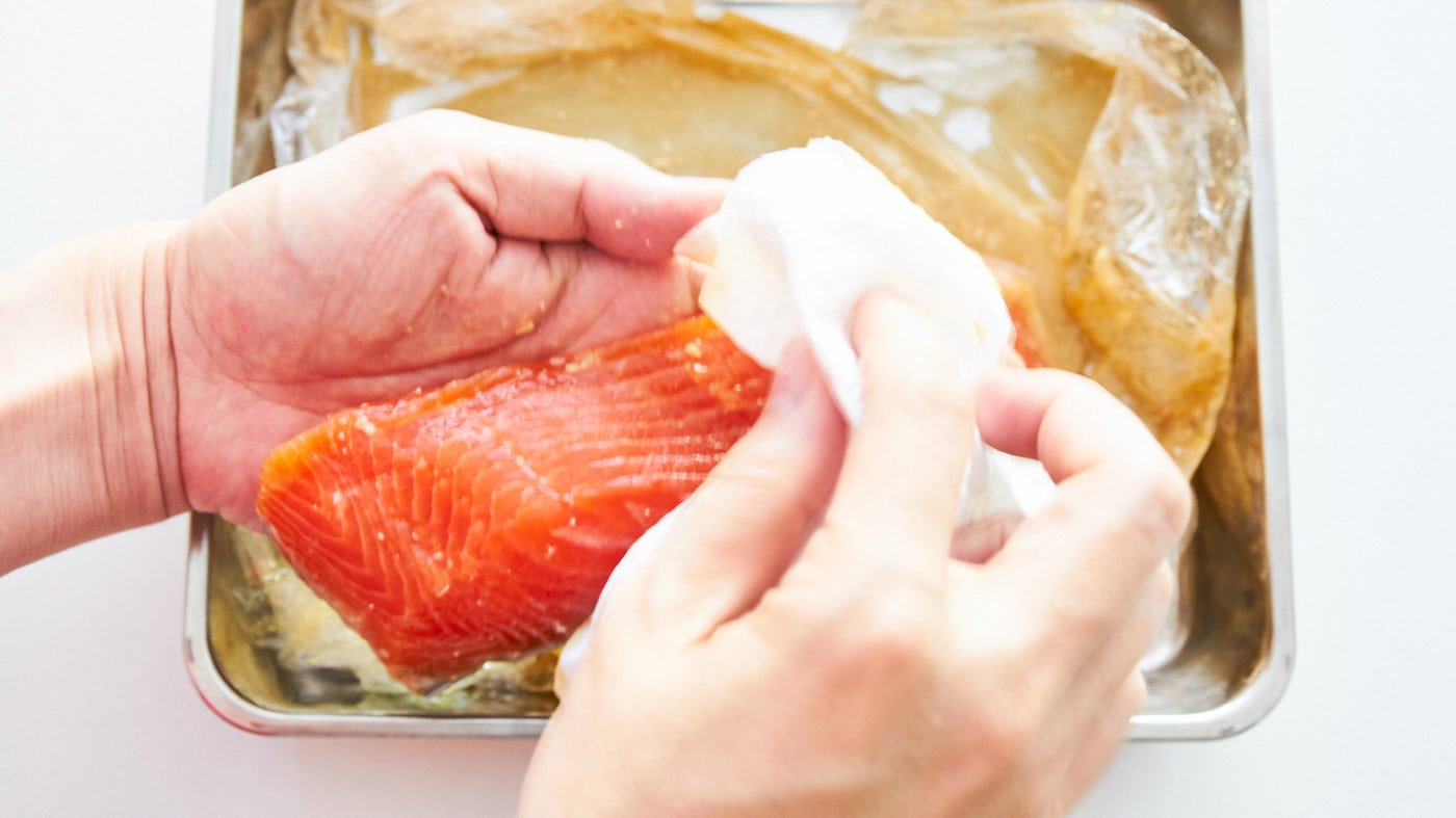 Removing the excess miso marinade from salmon fillets using paper towels.