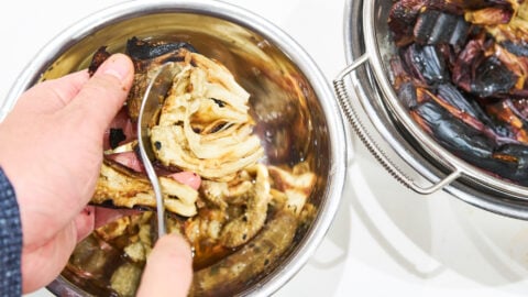 Scraping the flesh from char-roasted eggplant using a spoon for Mutabbal.