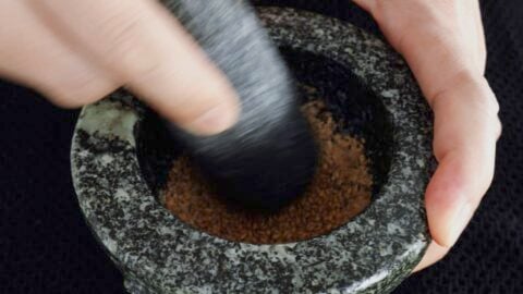 Grinding toasted sesame seeds with a mortar and pestle.