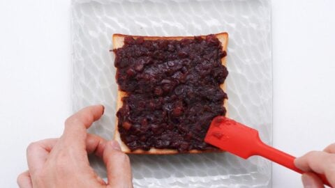 Spreading anko onto buttered toast with a spatula.