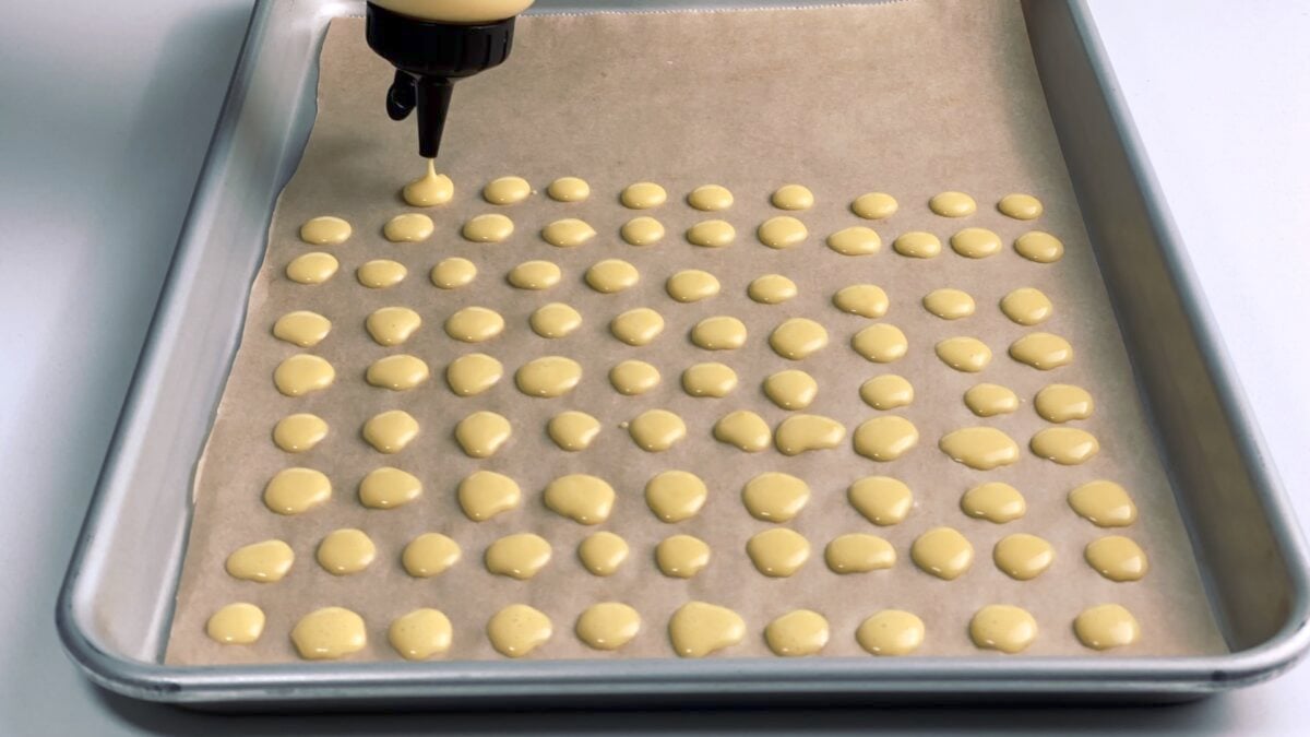 Making mini pancakes on a baking sheet with a squeeze bottle.