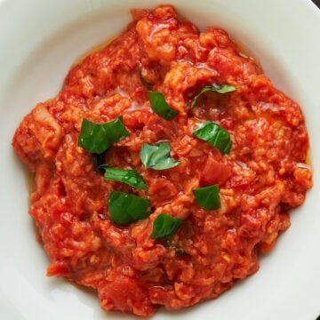 Pappa al Pomodoro (Tuscan Bread and Tomato Soup) in a white bowl on a dark surface with a fresh tomato and basil leaves.