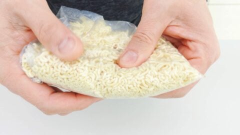 Crumbling instant ramen noodles in a plastic bag.