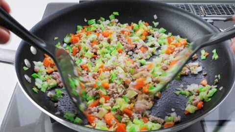 Stir-frying pork with cabbage, carrots, and onions in a frying pan with spatulas.