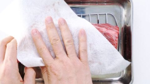 Patting wagyu beef dry with paper towels.