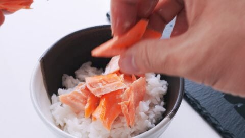 Flaking salmon on top of a bowl of rice.