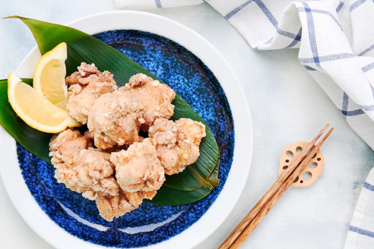 Crispy, juicy, and flavorful chicken karaage served with wedges of lemon on a bed of bamboo leaves.