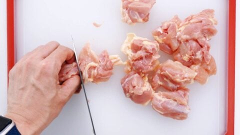 Cutting chicken thighs up into bite-sized pieces.