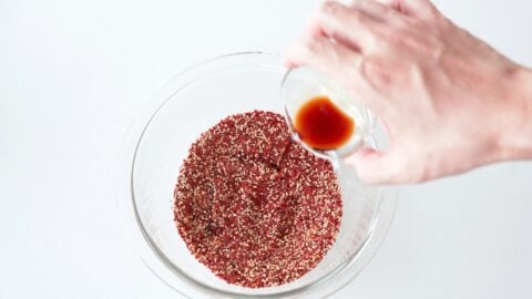 Adding soy sauce to chili pepper mixture in a glass bowl.