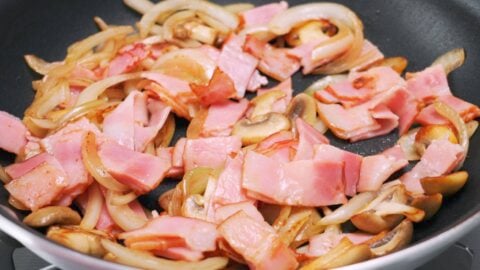 Bacon mushrooms and onions in a frying pan.